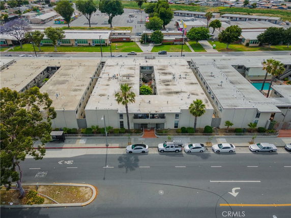 Aerial view of a large building complex with flat rooftops, situated along a road with parked cars.