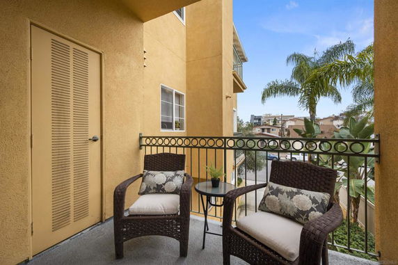 Balcony with chairs and small table, view of nearby buildings and palm trees.