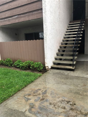 View of a building entrance with outdoor stairs and a small fenced area.