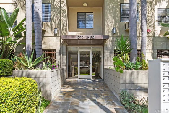 Front view of a multi-story building entrance with plants and glass doors.