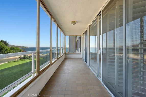 Enclosed outdoor area with large glass windows offering a view of the sea and greenery.