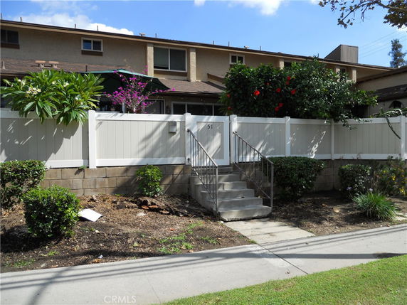 Front view of a two-story house with beige siding and a white fence.
