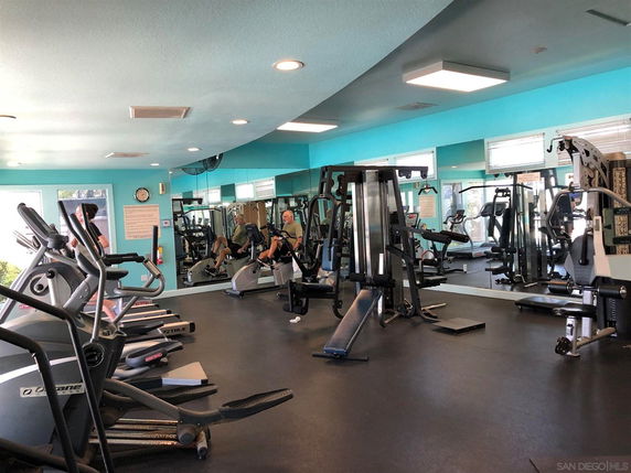 Indoor gym area with various exercise equipment and mirrors on the walls.