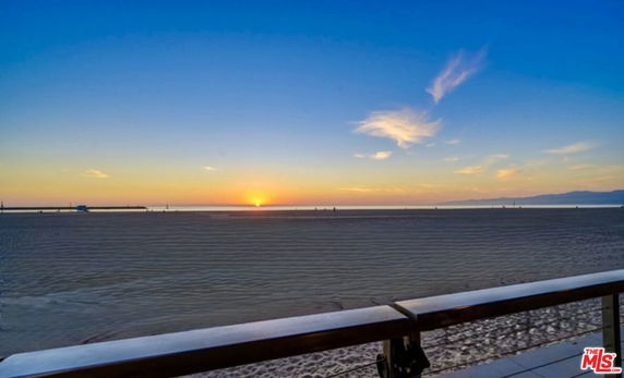 Panoramic view of a sunset over the ocean with visible sand and horizon.
