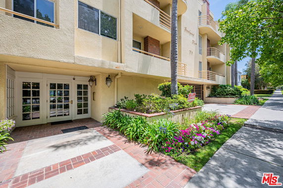 Front view of a multi-story residential building with balconies and landscaped entrance.