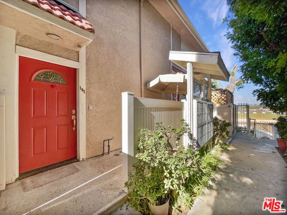 Front view of a building entrance with a red door and a small patio area.