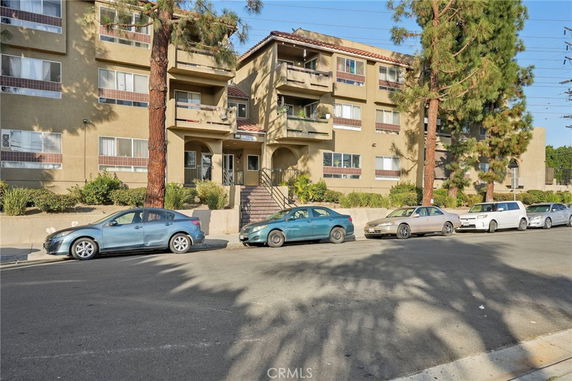 Front view of a multi-story apartment building with balconies and an entrance staircase.