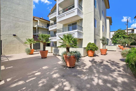 Front view of a multi-story residential building with balconies and potted plants.
