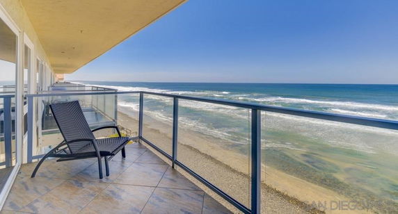 Balcony with glass railing overlooking the ocean and beach.