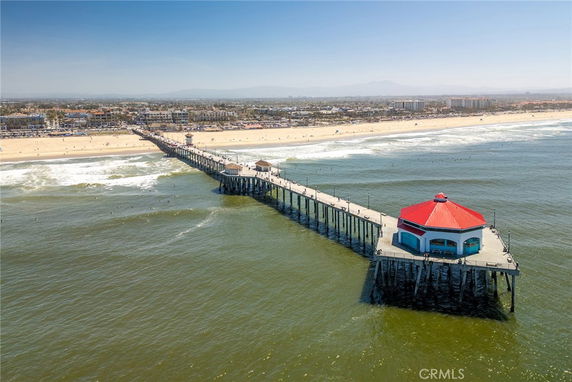 Panoramic view of a pier extending into the ocean with a red-roofed building at the end, beach and cityscape visible in the background.