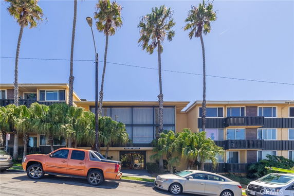 Front view of a multi-story building with balconies and surrounding palm trees.