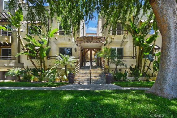 Front view of a multi-story building with stairway entrance and lush greenery.