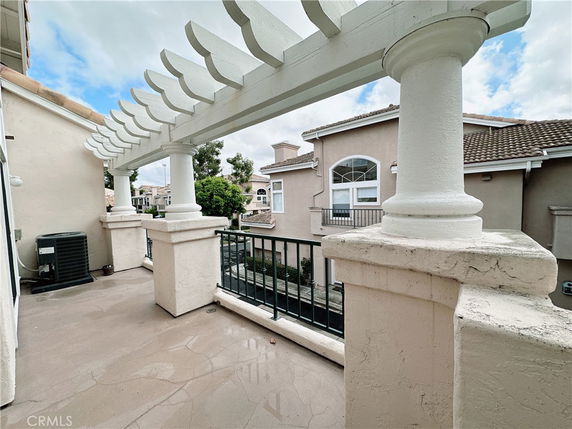 View from a balcony with white pillars and a pergola, overlooking nearby buildings.