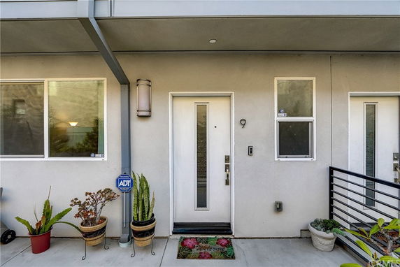 Front view of a modern building entrance with white door and windows, decorated with potted plants.