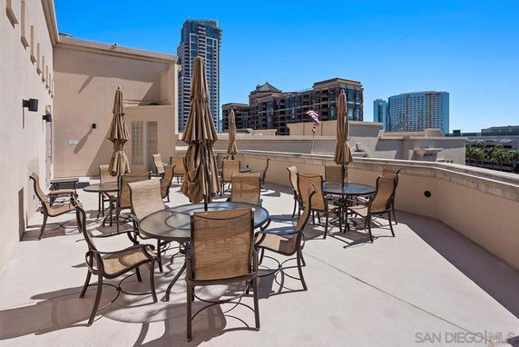 Rooftop seating area with round tables and chairs, and umbrellas, in an urban setting.