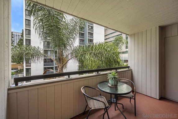 Outdoor balcony with a round table and two chairs, overlooking nearby buildings and palm trees.