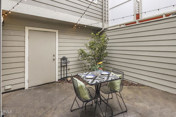 Small outdoor patio area with a table set and decorative lights.