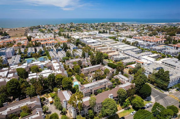 Aerial view of a residential area with buildings and trees, overlooking the ocean in the background.