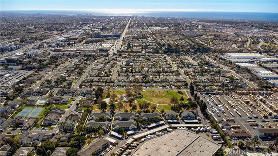 Panoramic aerial view of a sprawling urban area with houses, roads, parks, and distant ocean.