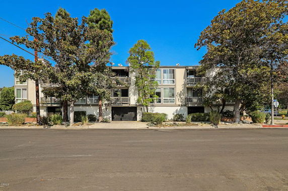 Front view of a three-story building with trees and balcony railings.