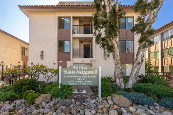 Front view of a multi-story condominium building with a sign and landscaping in front.