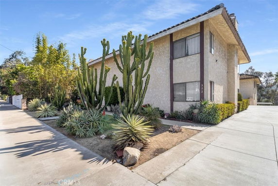Front view of a two-story house with a tiled roof and large cactus plants in the front yard.
