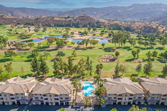 Panoramic view of a golf course with hills in the background and apartment buildings with a swimming pool in the foreground.