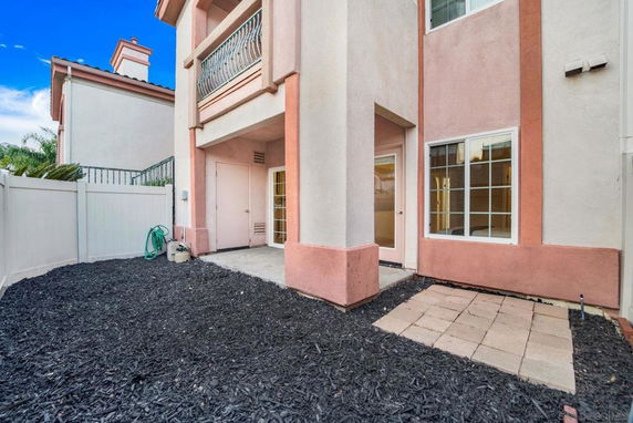 Backyard view of a multi-story house with beige and pink exterior, featuring a patio and fenced area.