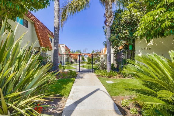 Walkway leading to group of buildings with orange tiled roofs and gated entrance.