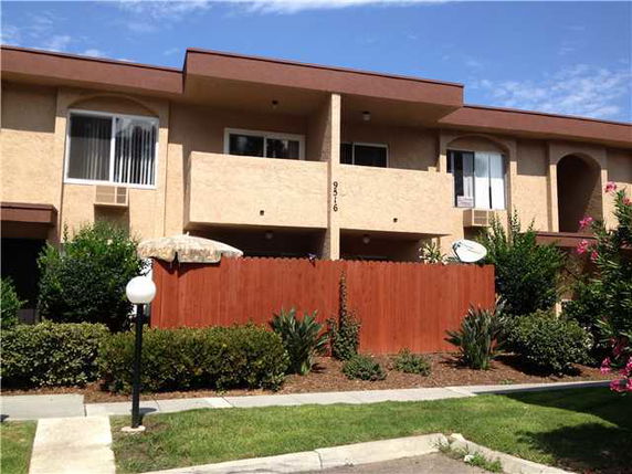 Front view of a multi-story building with balconies and a wooden fence.