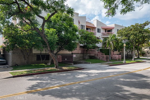 Front view of a multi-story residential building with balconies and surrounding trees.