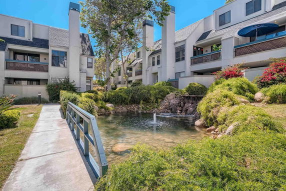 View of residential buildings with a small pond and greenery in front.