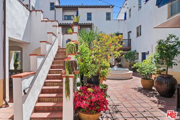 Exterior view of a building courtyard with a staircase, plants, and a fountain.