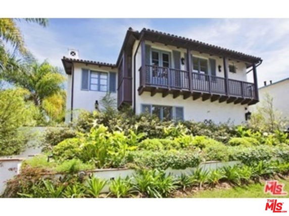 Front view of a multi-story house with a balcony and a garden.