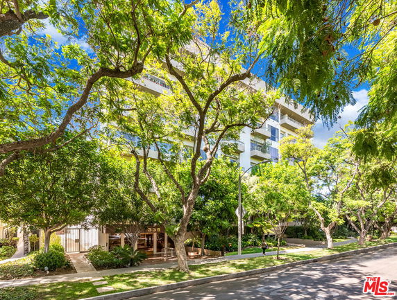 Front view of a multi-story residential building with balconies surrounded by trees.