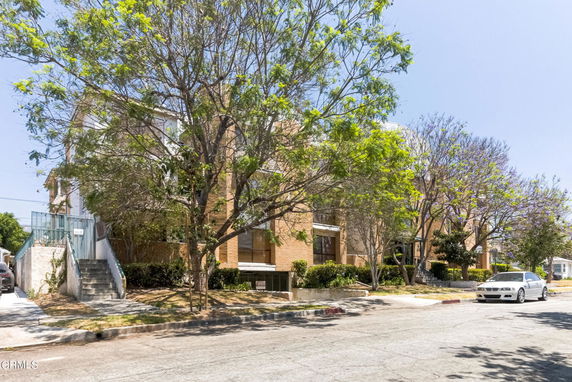 Front view of a multi-story brick apartment building with trees in the foreground.