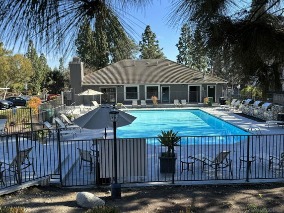 Swimming pool area in front of a building surrounded by trees and outdoor seating.