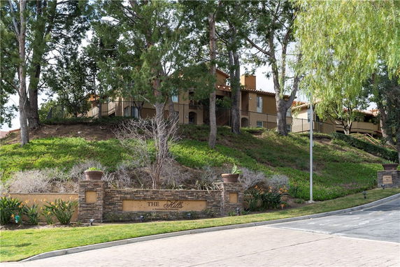 Front view of a multi-story building on a hillside with trees and a sign at the entrance.