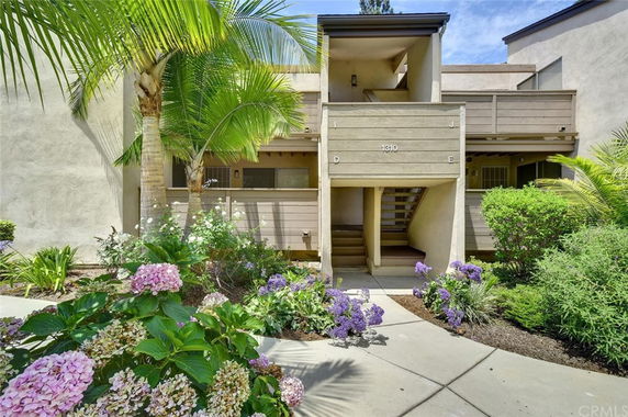Front view of a two-story building with an entrance stairway and surrounding plants.