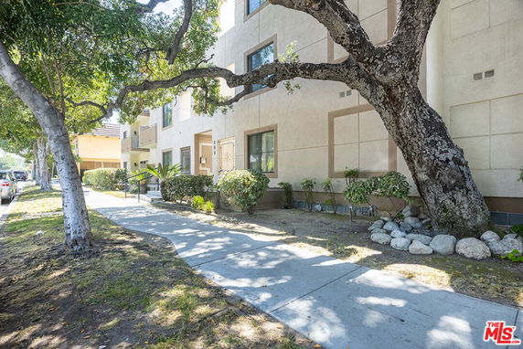 Front view of a multi-story residential building with a pathway and trees.