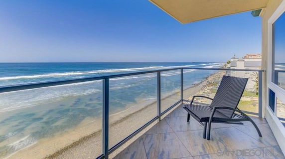 Panoramic view of the ocean from a balcony with a chair and glass railing.