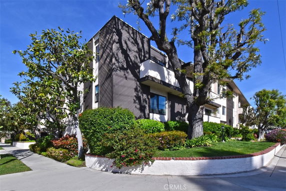 Front view of a multi-story building with balconies and surrounding trees.