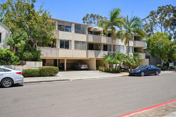 Front view of a multi-story apartment building with balconies and parking spaces.