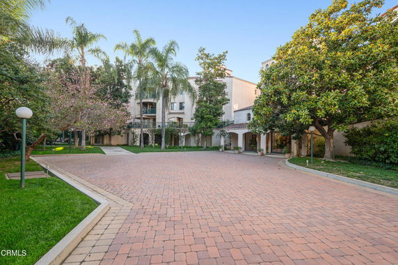 Front view of a multi-story building with a paved courtyard and surrounded by trees.