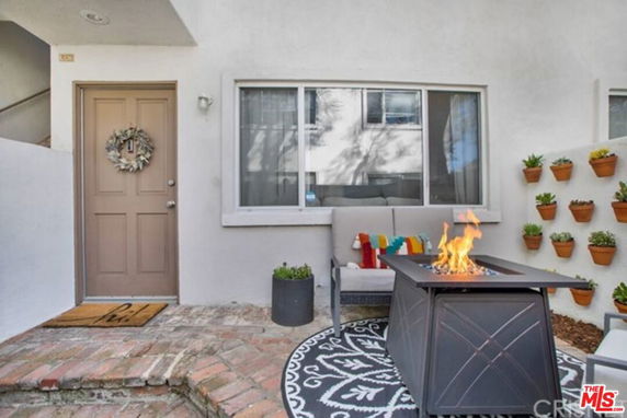 Front view of a house entrance with a brown door and window, featuring a decorative wreath and outdoor seating with a fire table.
