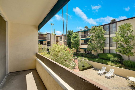 Balcony view of garden area with lounge chairs and surrounding apartment buildings.