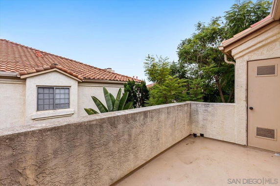 Rooftop area with stucco walls and a view of red-tiled roofs and surrounding greenery.