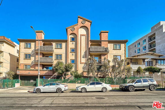 Front view of a multi-story apartment building with balconies and a distinctive central roof structure.