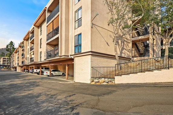 Front view of a multi-story apartment building with balconies and a covered parking area.