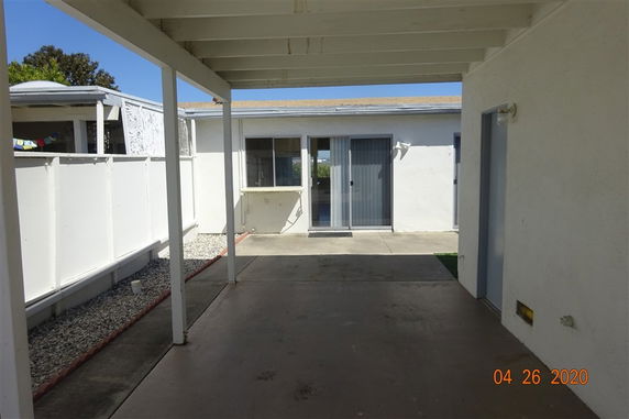 Backyard view of a house with a covered patio and sliding glass doors.